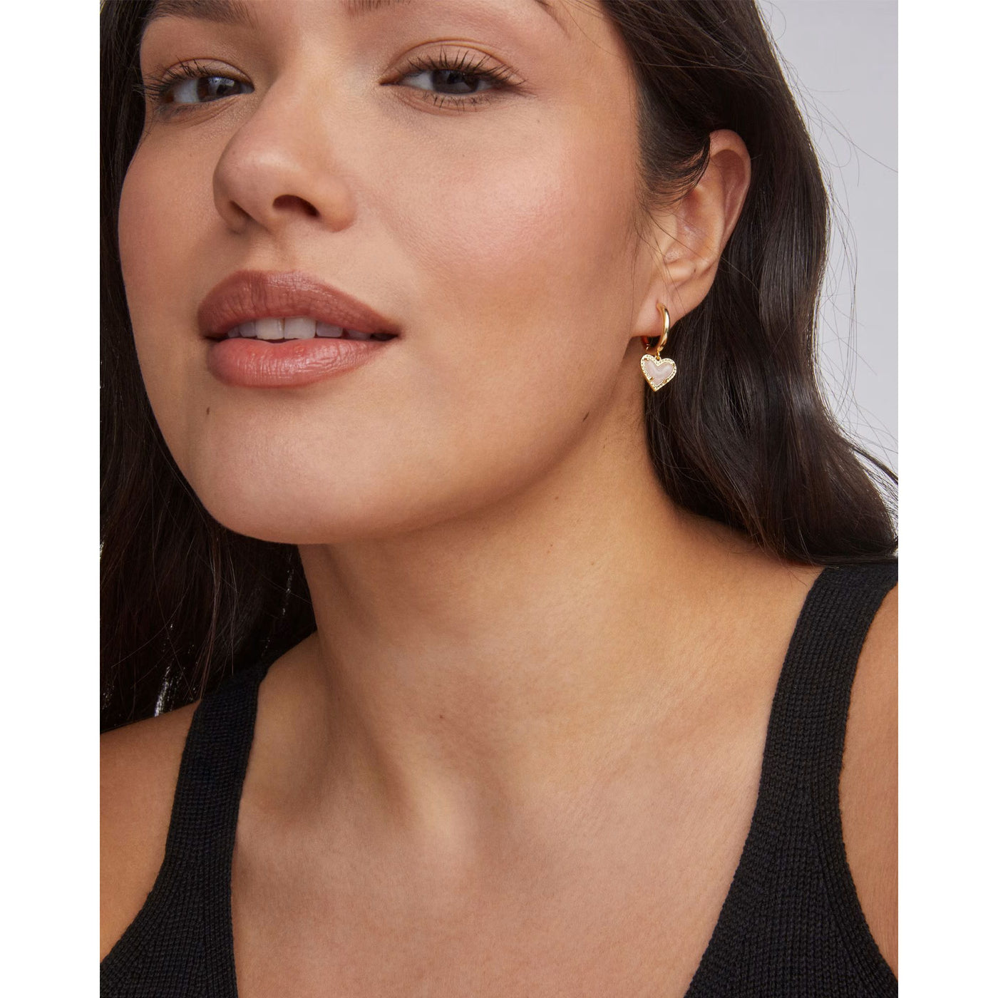 Close-up of a woman wearing heart-shaped earrings with a plain background